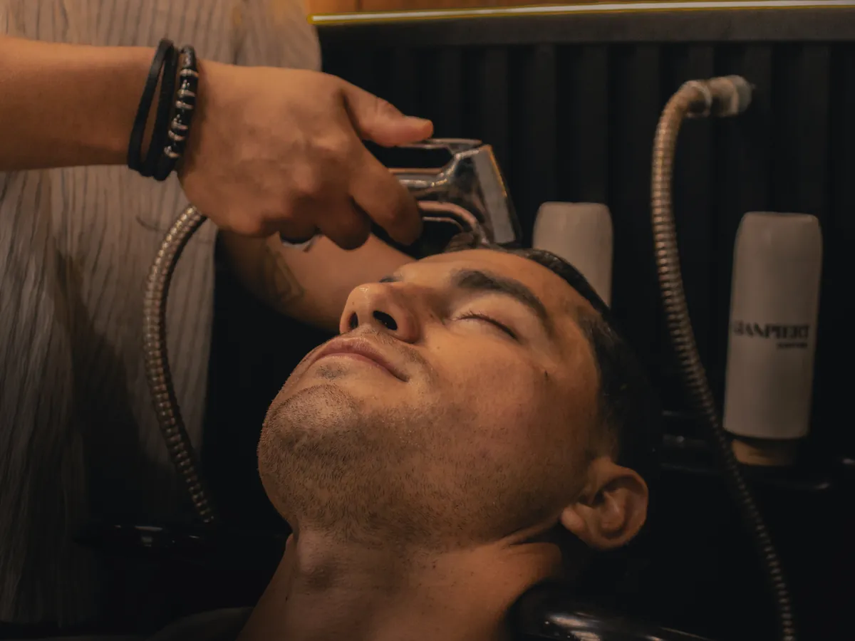Cliente relajado durante el lavado capilar en la barbería